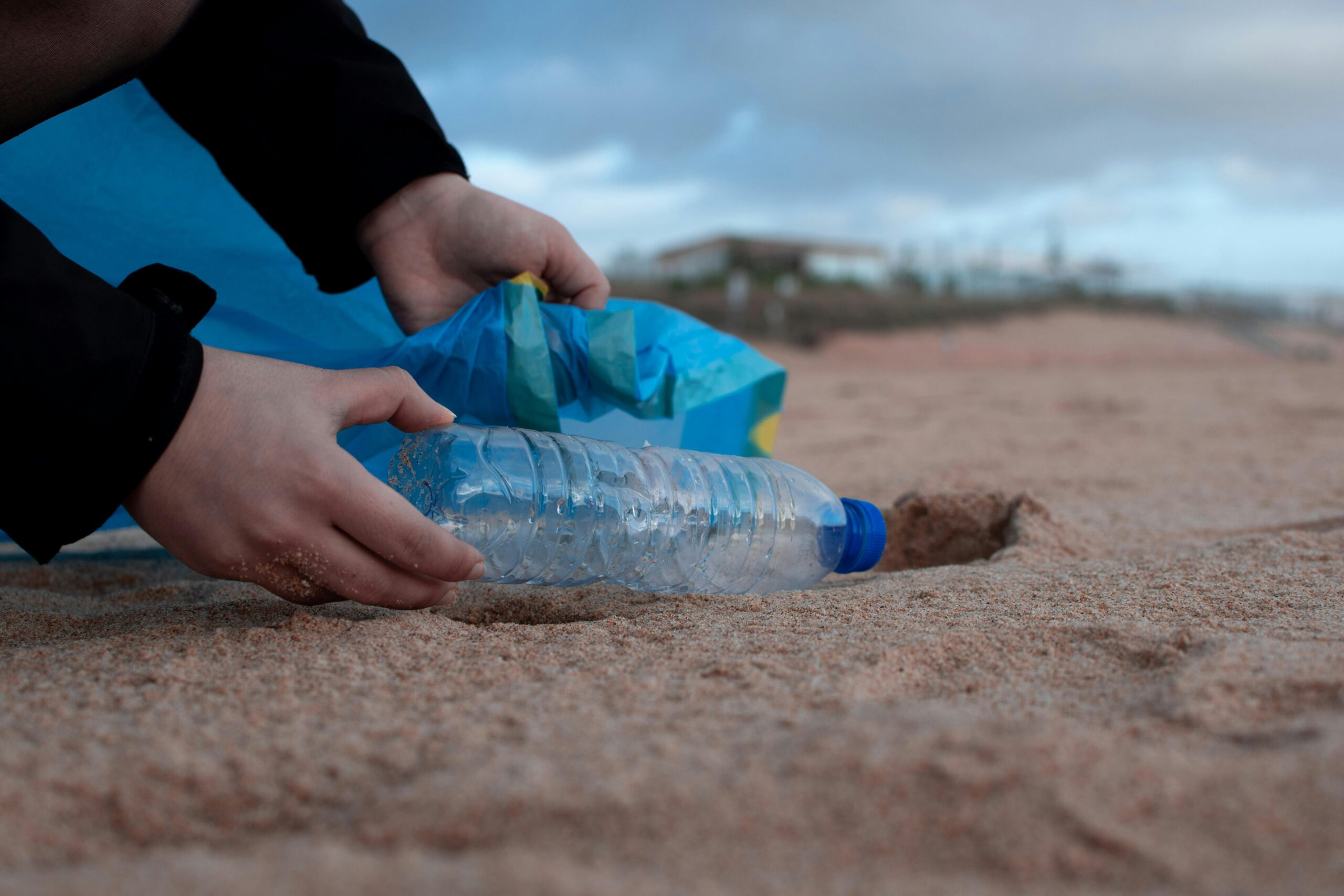 Hand picking up plastic bottle from the beach
